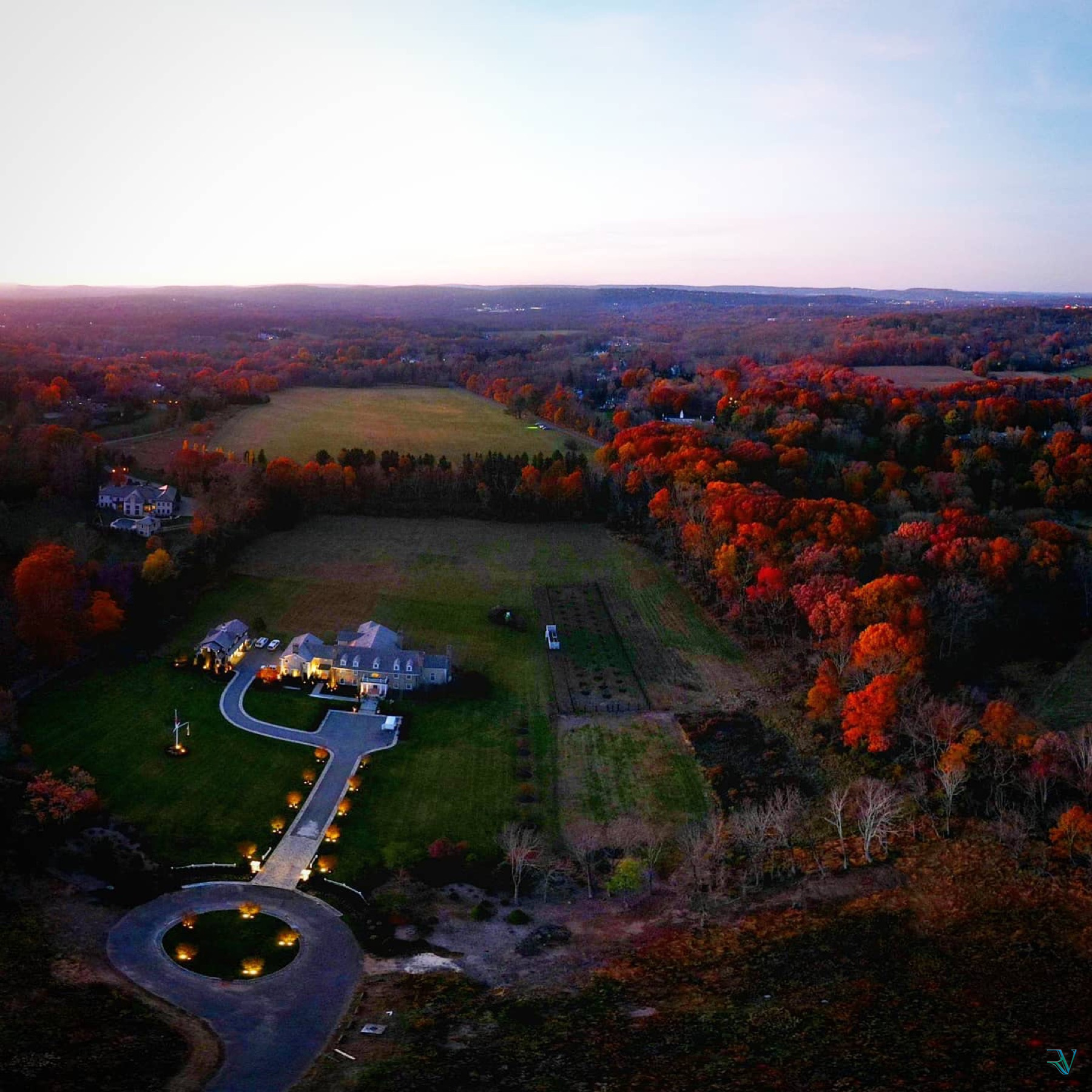 Aerial view of a country estate surrounded by autumn fields and forest at dusk