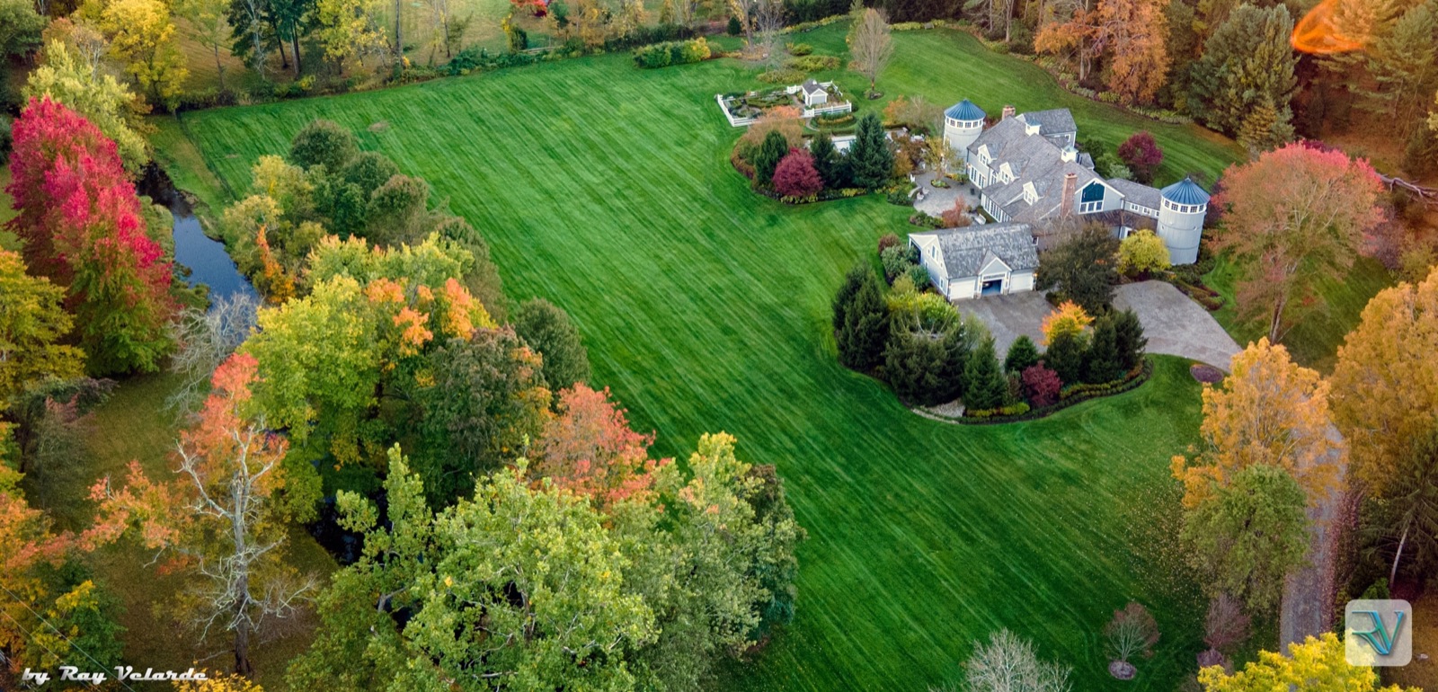 Aerial view of a large estate, green lawn, pond, and surrounding autumn trees