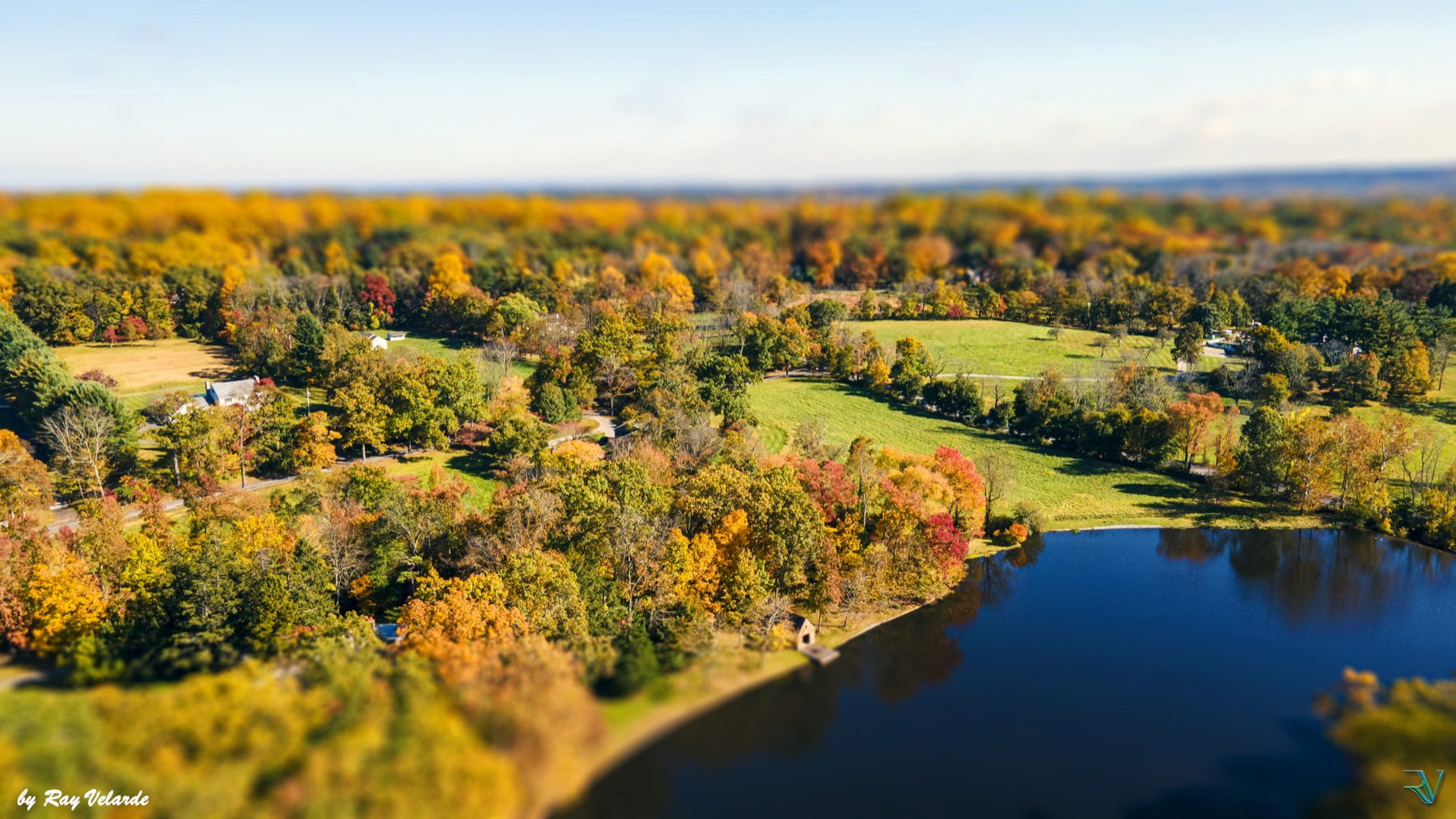 Aerial tilt-shift view of autumn fields, colorful trees, and a deep blue lake