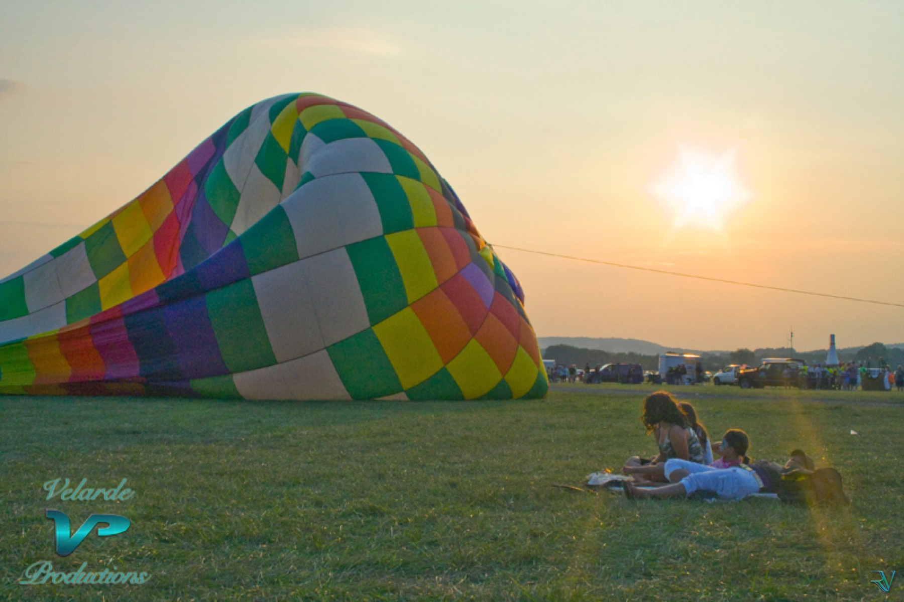 Colorful hot-air balloon resting on grass as people watch the sunset