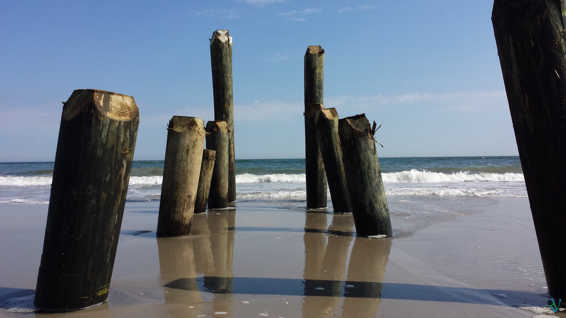 Weathered wooden pilings reflected in wet sand beside ocean waves