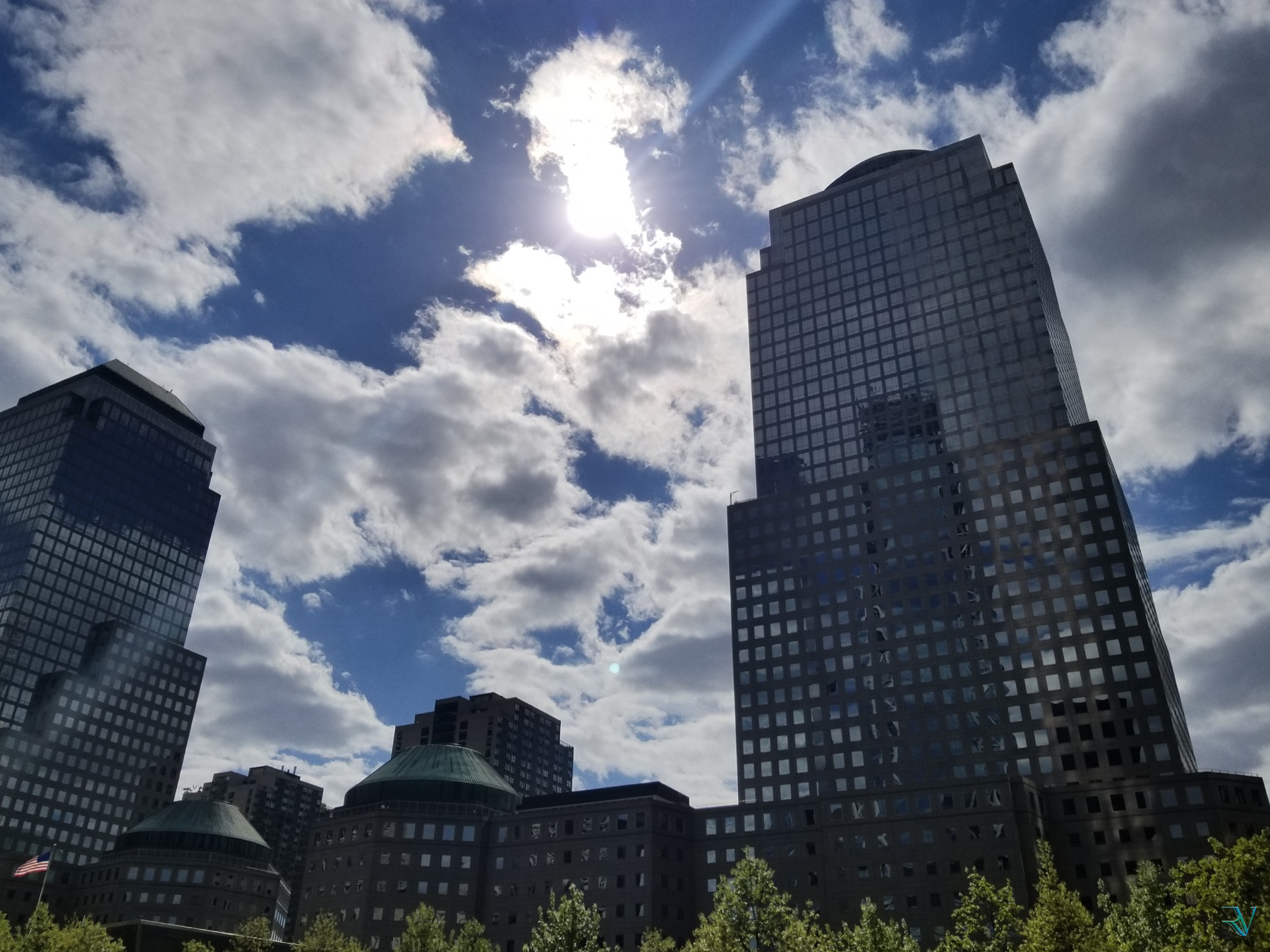 Sun and dramatic clouds framed by tall buildings in Lower Manhattan