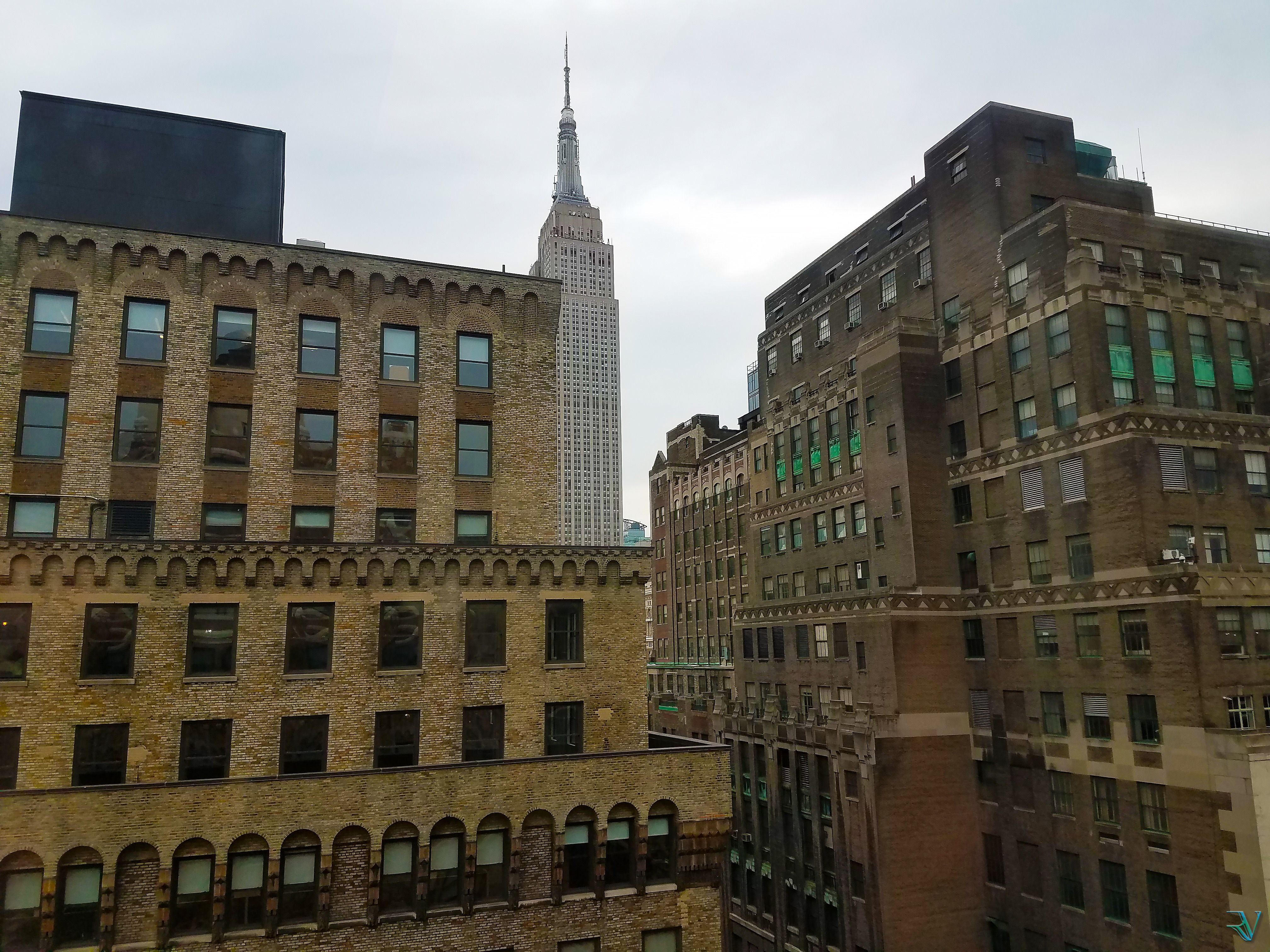 Empire State Building rising between warm brick buildings in Manhattan