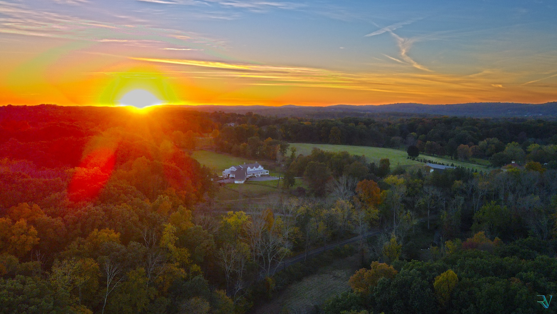 Intense orange sunset spilling across a wooded ridge and country fields