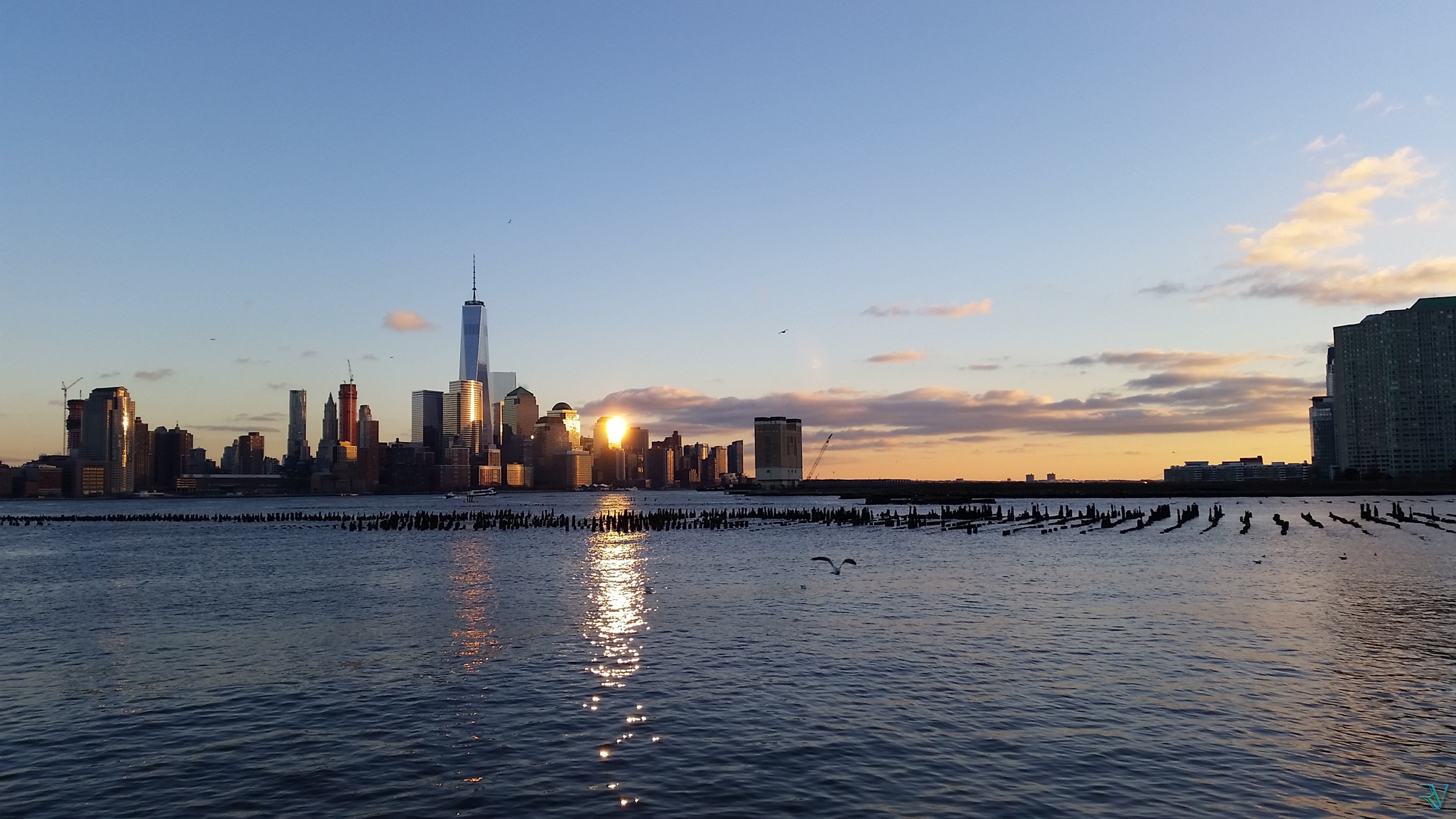 Sun setting between Lower Manhattan towers and reflecting across the Hudson River