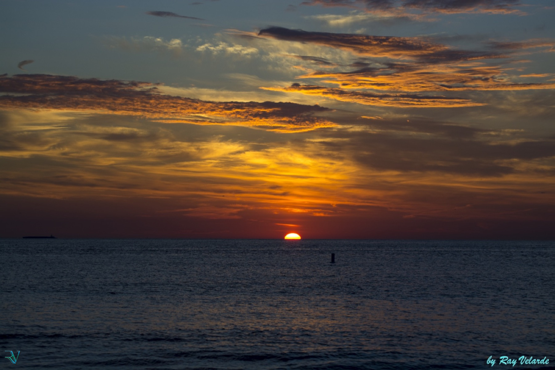 Deep orange sunrise beneath layered clouds over the ocean