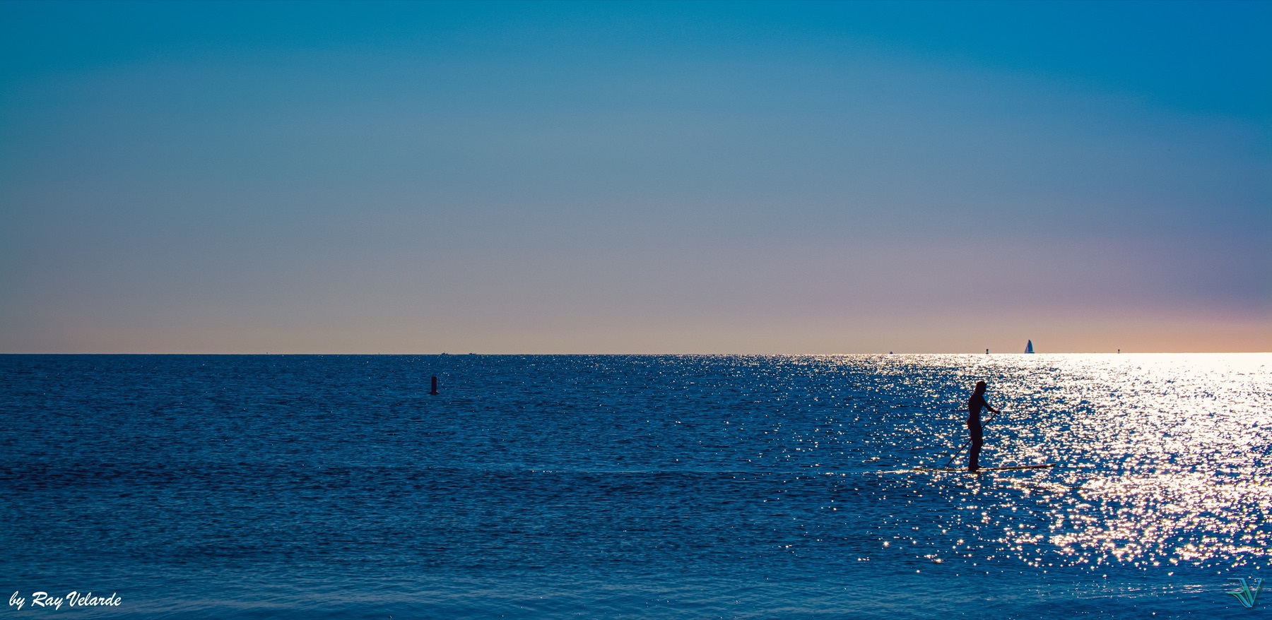 Silhouette of a paddleboarder moving across sunlit blue water