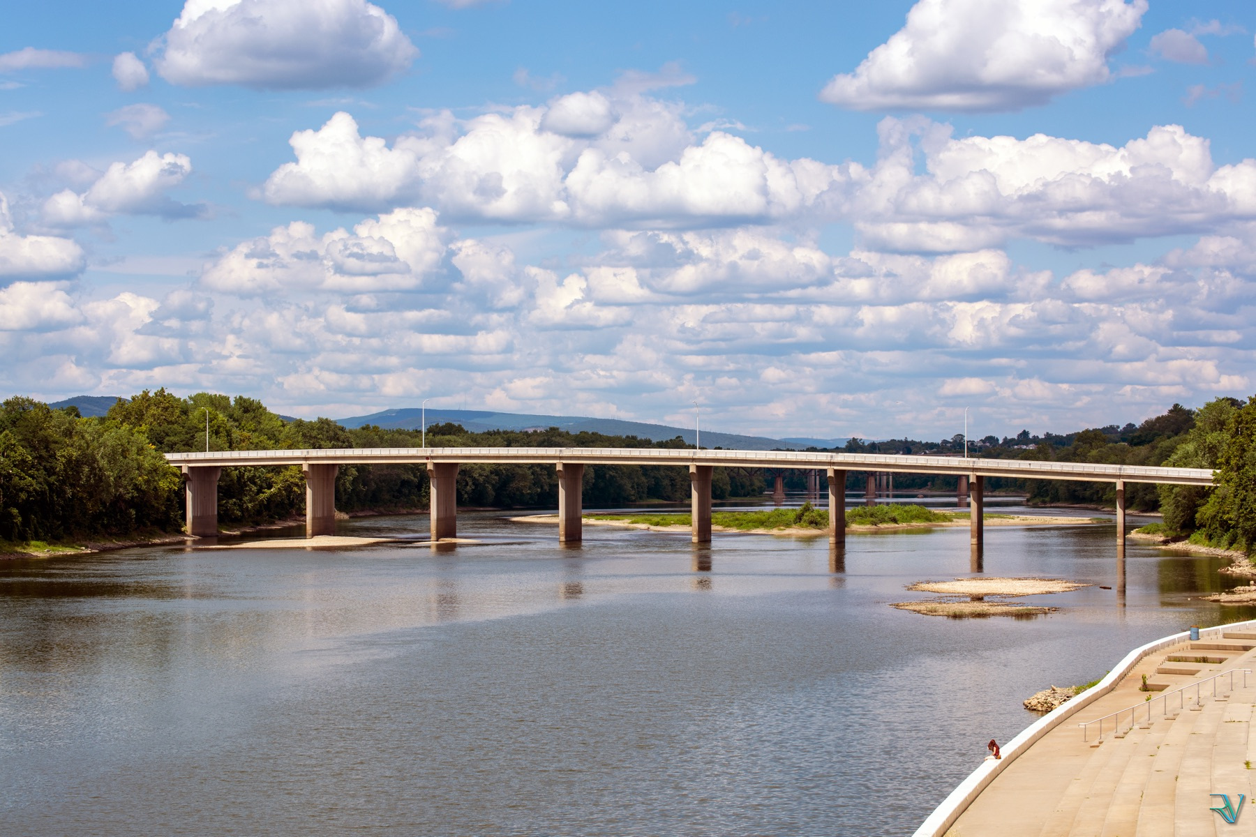 Bridge spanning a calm river beneath a field of bright white clouds