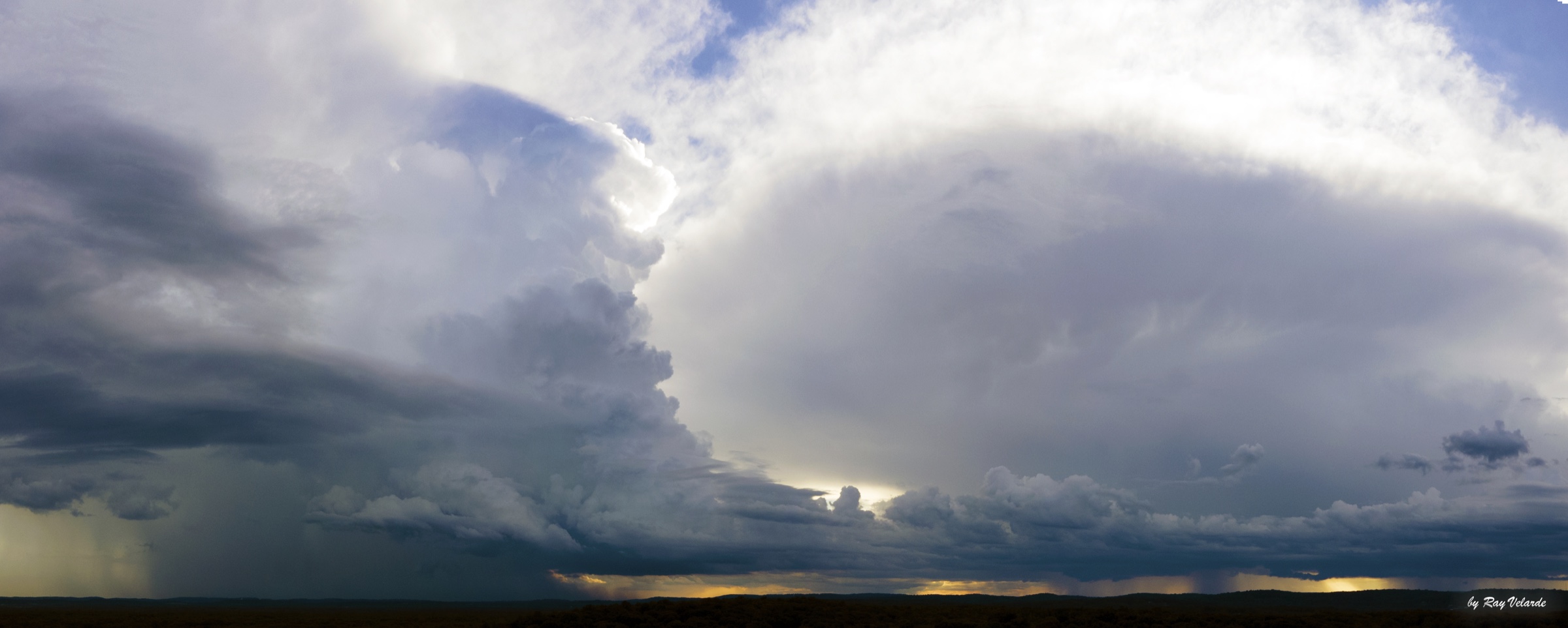 Panoramic storm front with massive layered clouds and distant curtains of rain