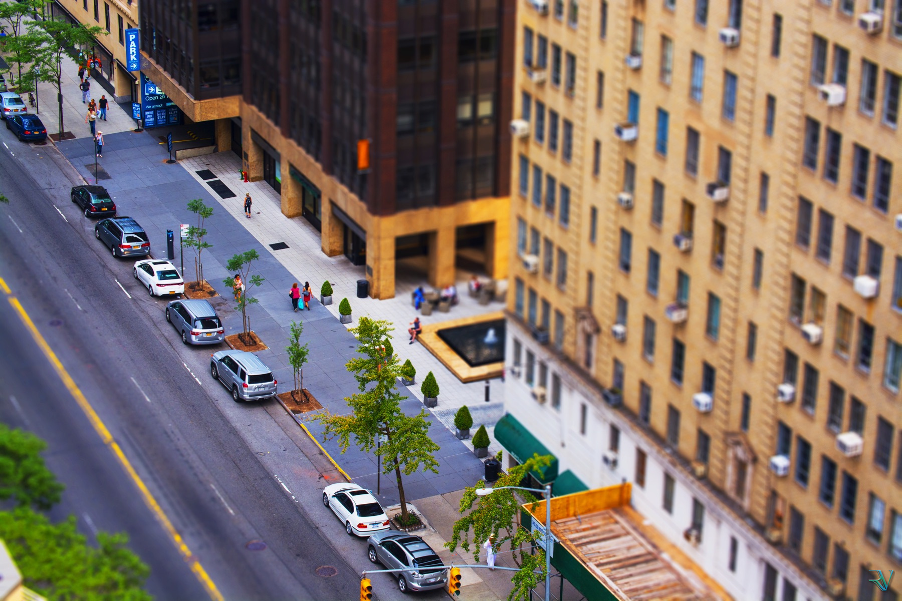 Tilt-shift style overhead view of people, cars, and buildings on a city street