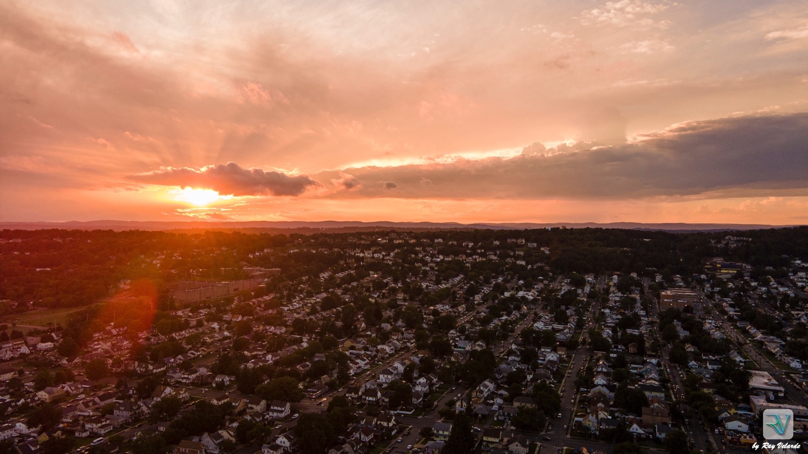 Aerial sunset over a suburban neighborhood and distant wooded hills