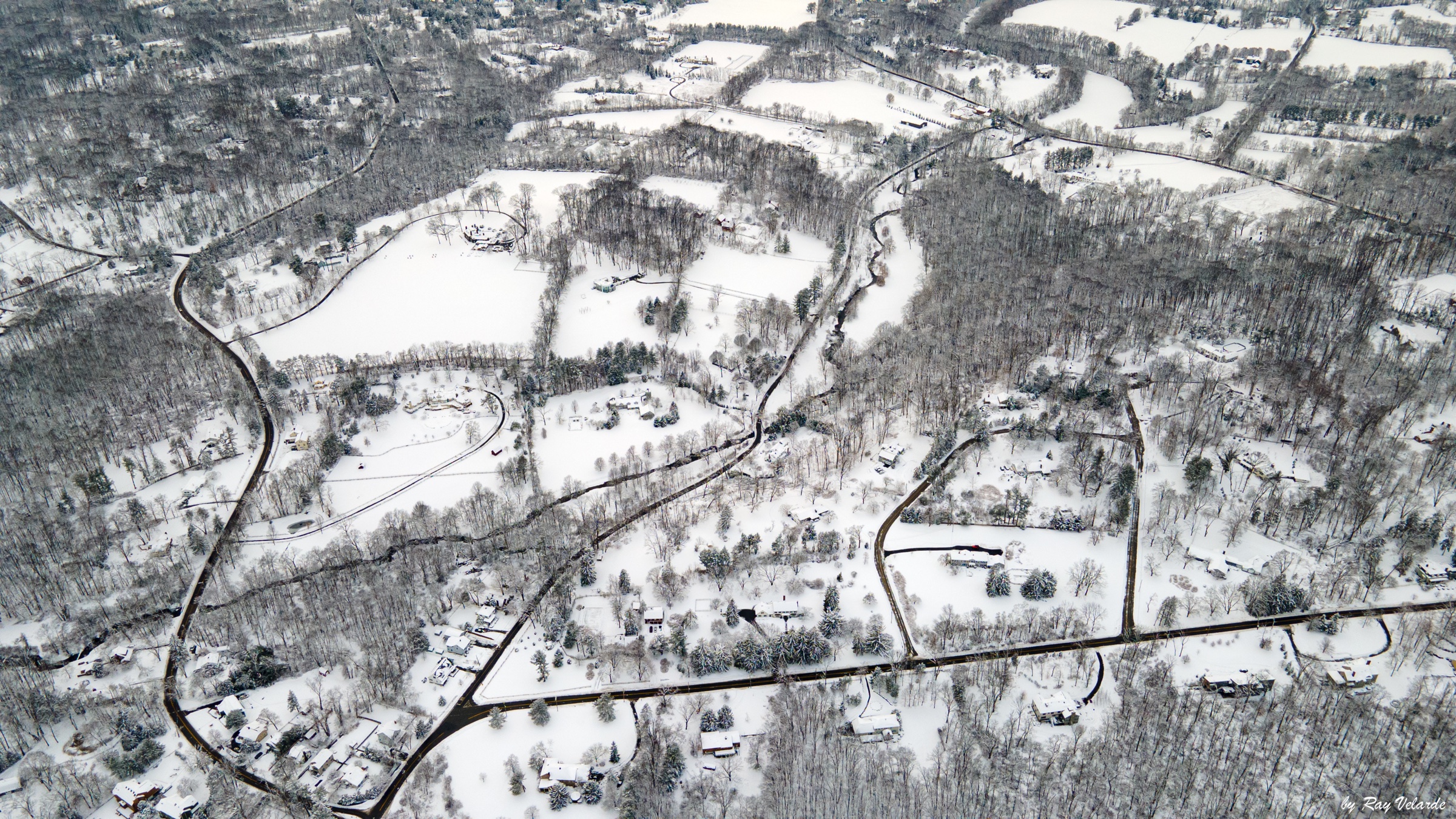 High aerial view of curving roads, homes, and woodland covered in fresh snow